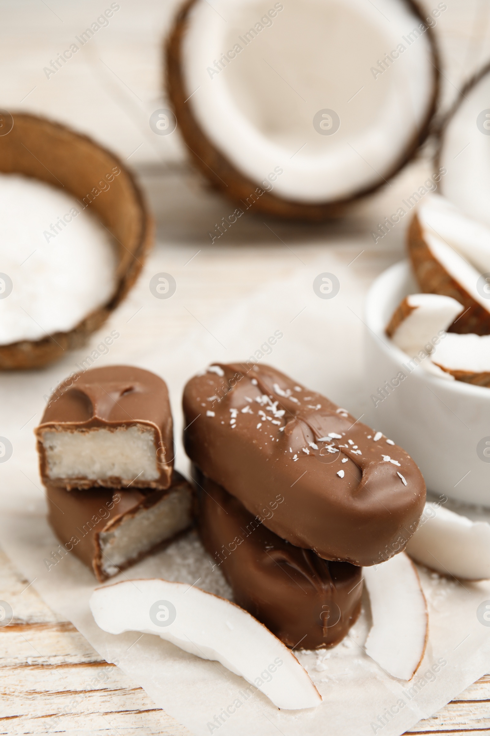 Photo of Delicious milk chocolate candy bars with coconut filling on white wooden table, closeup. Space for text