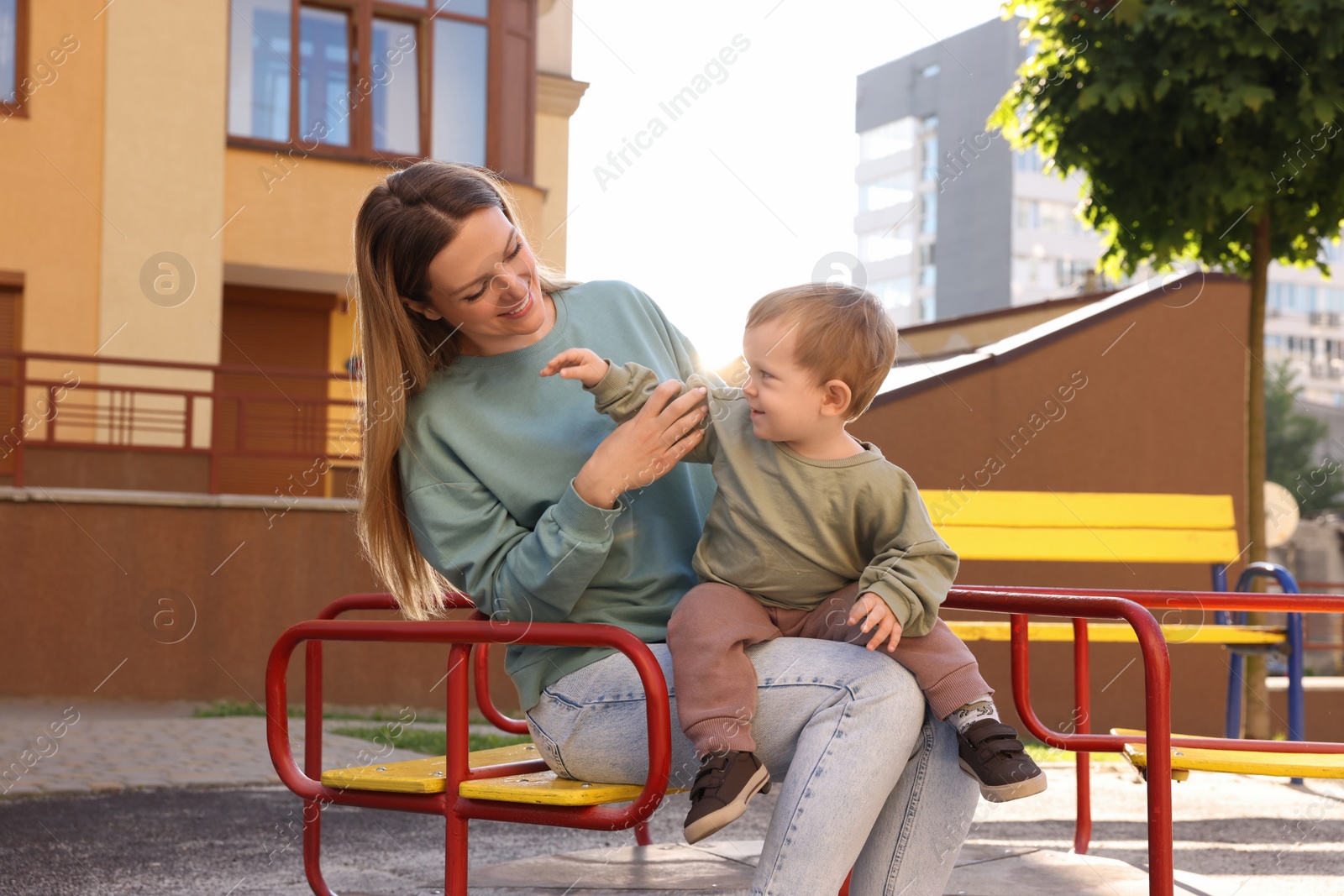 Photo of Happy nanny with cute little boy sitting on carousel outdoors