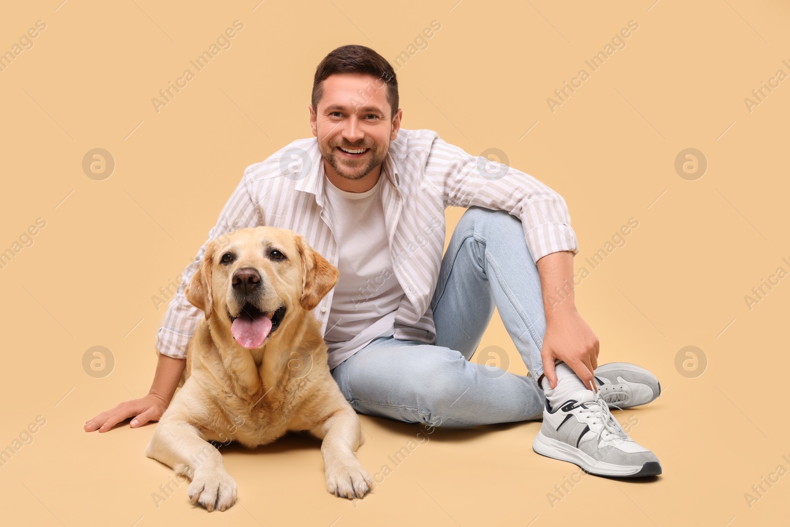 Photo of Man with adorable Labrador Retriever dog on beige background. Lovely pet