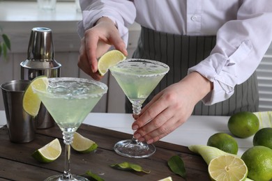 Photo of Bartender putting piece of lime onto glass with delicious Margarita cocktail at wooden table, closeup