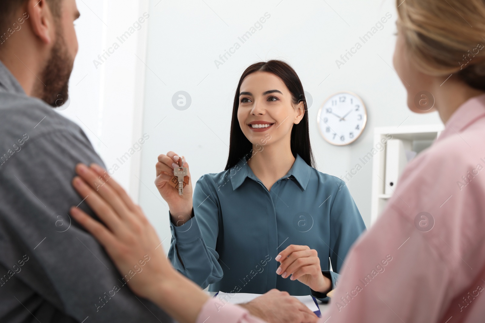 Photo of Real estate agent giving new house key to happy young couple in office