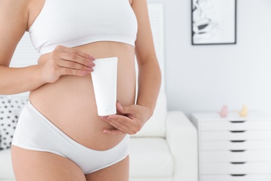 Pregnant woman holding body cream at home, closeup