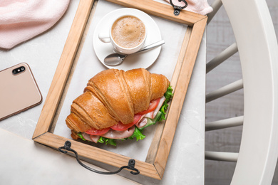 Photo of Tasty croissant sandwich and coffee on light grey marble table, flat lay