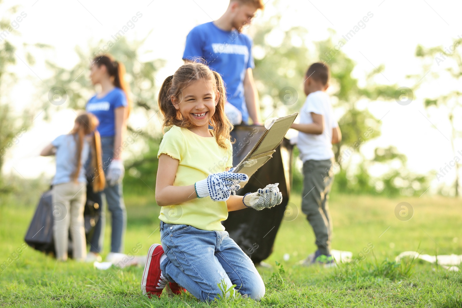 Photo of Little girl collecting trash in park. Volunteer project