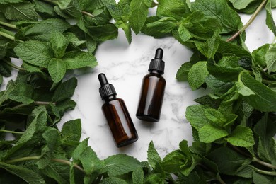 Photo of Bottles of mint essential oil and green leaves on white marble table, flat lay