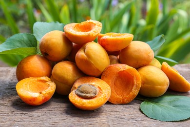 Photo of Delicious ripe apricots and green leaves on wooden table outdoors, closeup