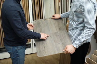 Photo of Men holding sample of wooden flooring in shop, closeup