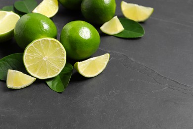 Photo of Fresh ripe limes and leaves on black table, closeup. Space for text