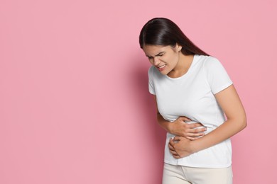 Photo of Young woman suffering from menstrual pain on pink background, space for text