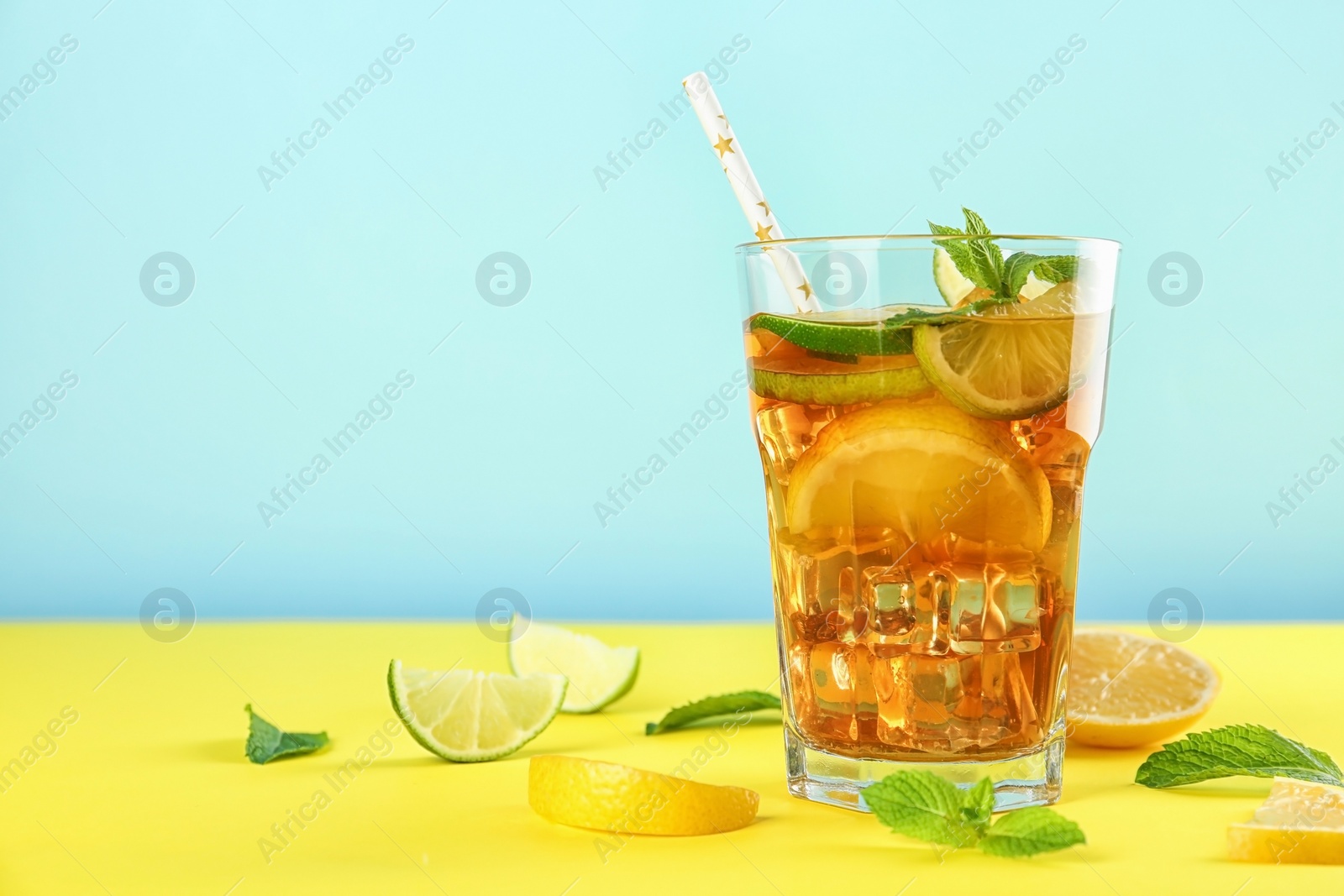 Photo of Glass of refreshing iced tea on yellow table against blue background. Space for text