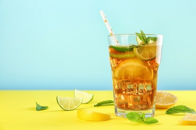Photo of Glass of refreshing iced tea on yellow table against blue background. Space for text