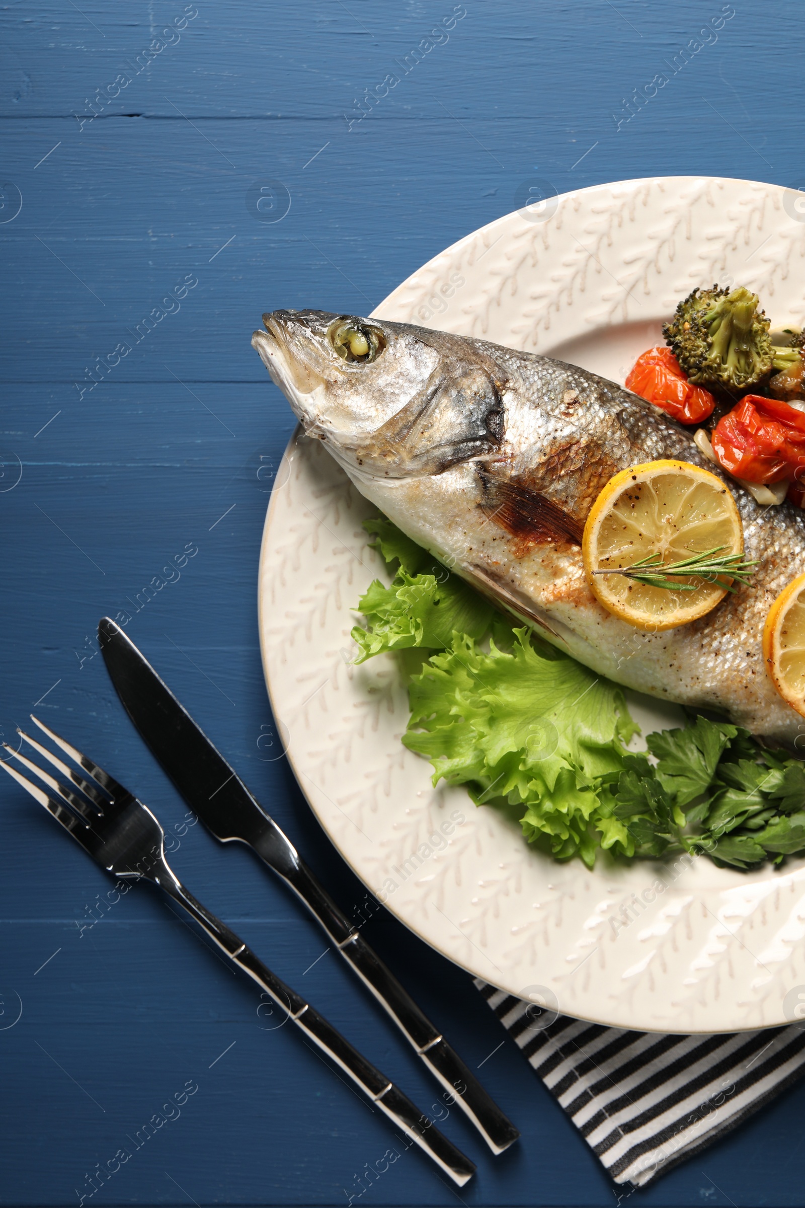 Photo of Delicious baked fish and vegetables served on blue wooden table, top view