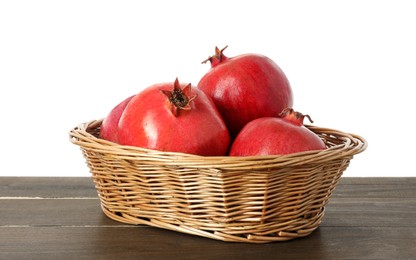 Fresh pomegranates in wicker basket on wooden table against white background