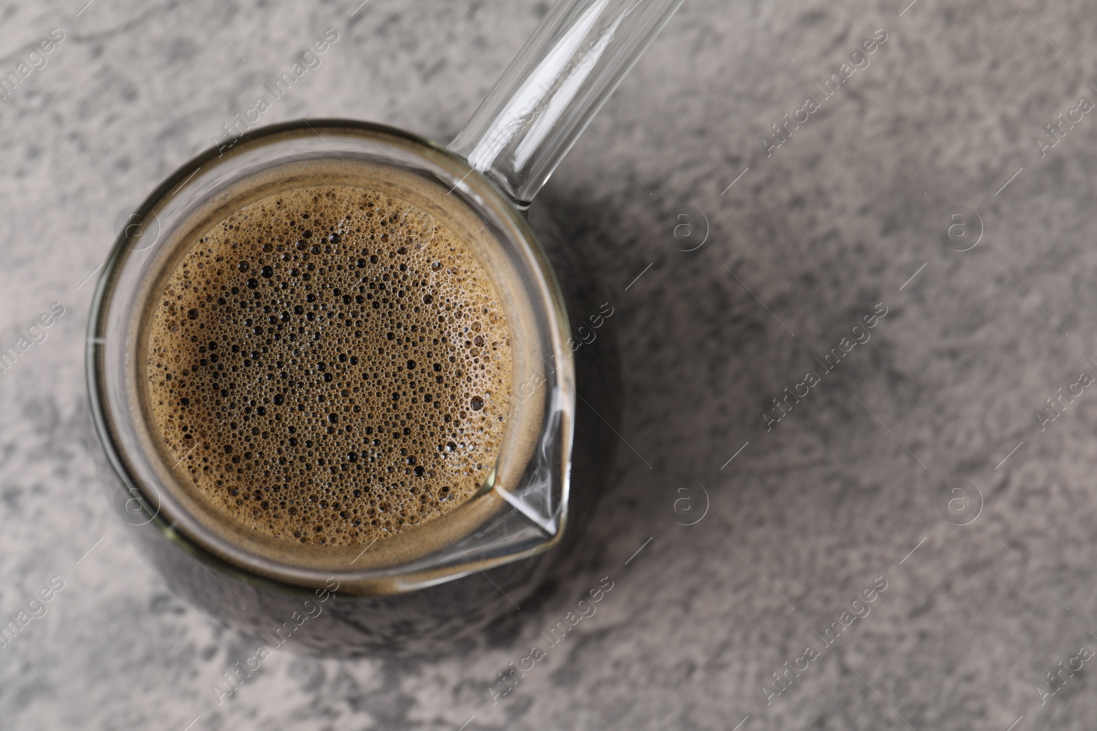 Photo of Turkish coffee in glass cezve on light grey table, top view. Space for text