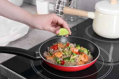 Photo of Woman squeezing lime into rice with shrimps and vegetables on induction stove, closeup