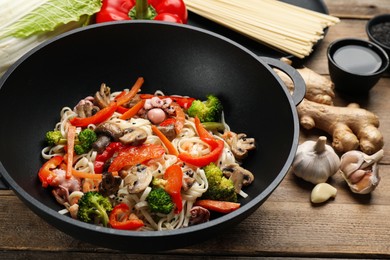 Photo of Stir fried noodles with seafood and vegetables in wok on wooden table