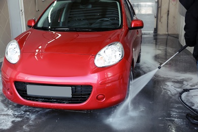 Worker cleaning automobile with high pressure water jet at car wash