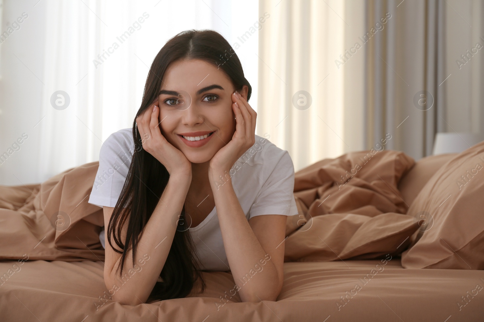 Photo of Young woman lying in bed with brown linens at home