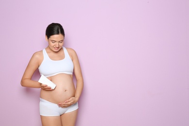 Photo of Pregnant woman holding body cream on color background with space for text