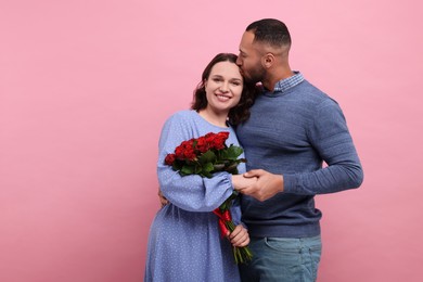 Photo of Happy couple celebrating Valentine's day. Beloved woman with bouquet of red roses on pink background, space for text