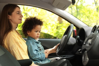 Photo of Mother with cute little daughter driving car together. Child in danger