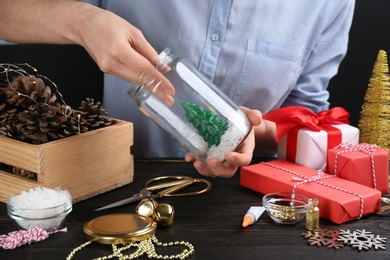 Photo of Woman making snow globe at black wooden table, closeup