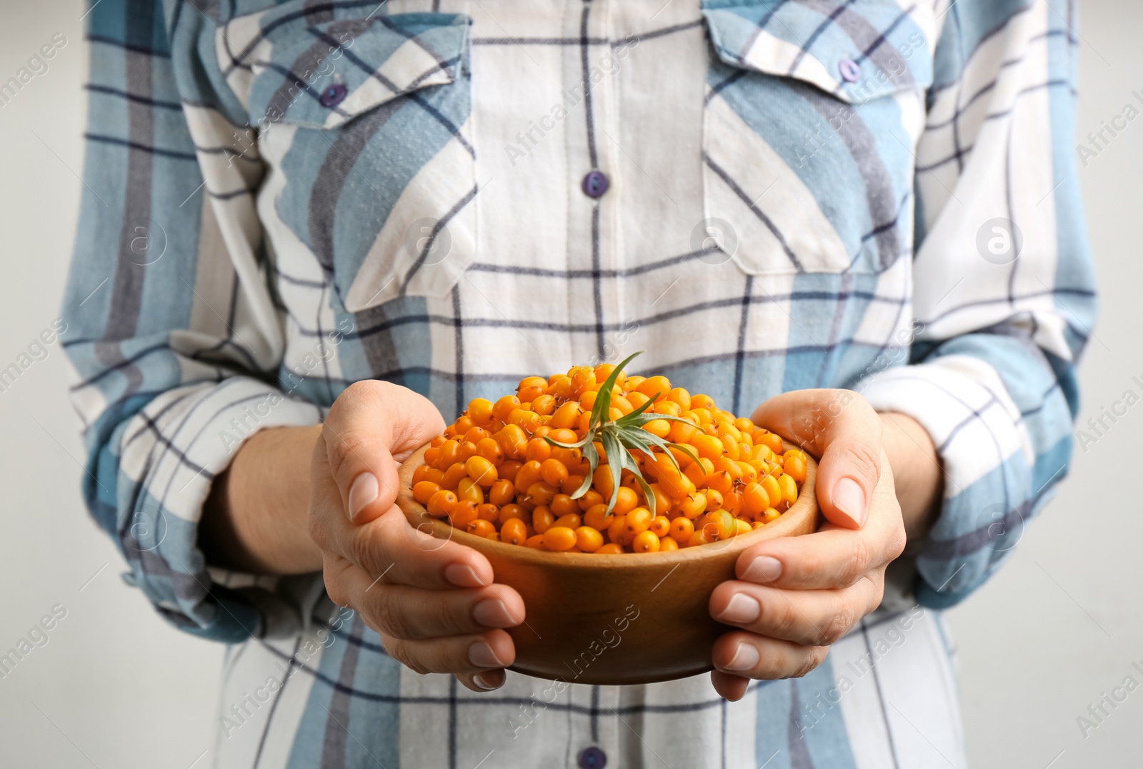 Photo of Woman holding bowl with fresh ripe sea buckthorn on light background, closeup