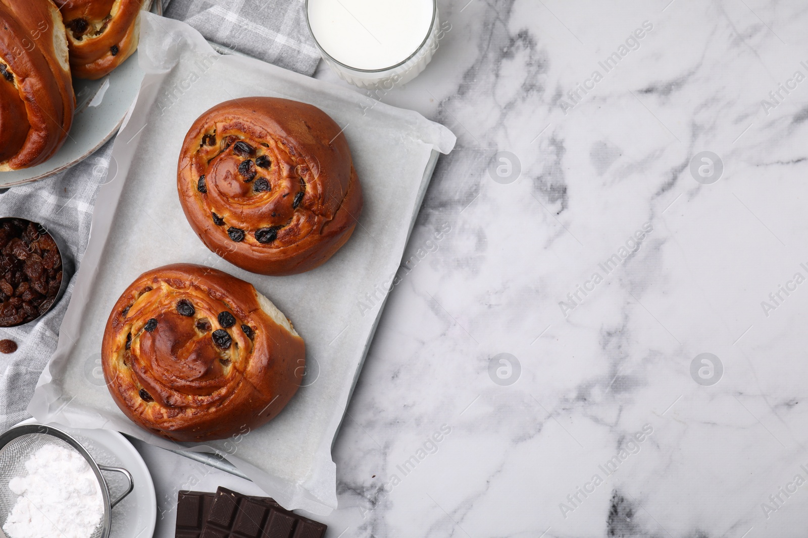 Photo of Delicious rolls with raisins on white marble table, flat lay and space for text. Sweet buns