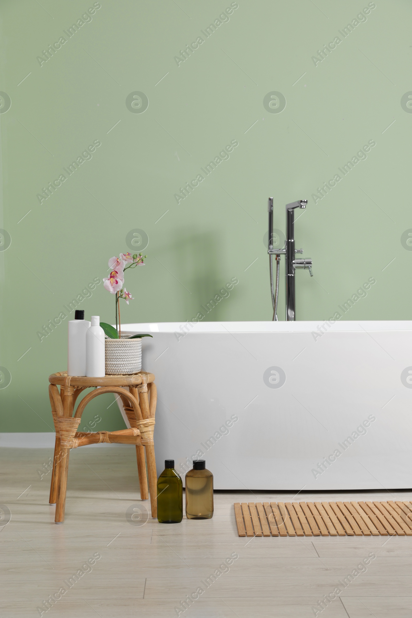 Photo of Stylish bathroom interior with ceramic tub, care products and beautiful orchid on coffee table