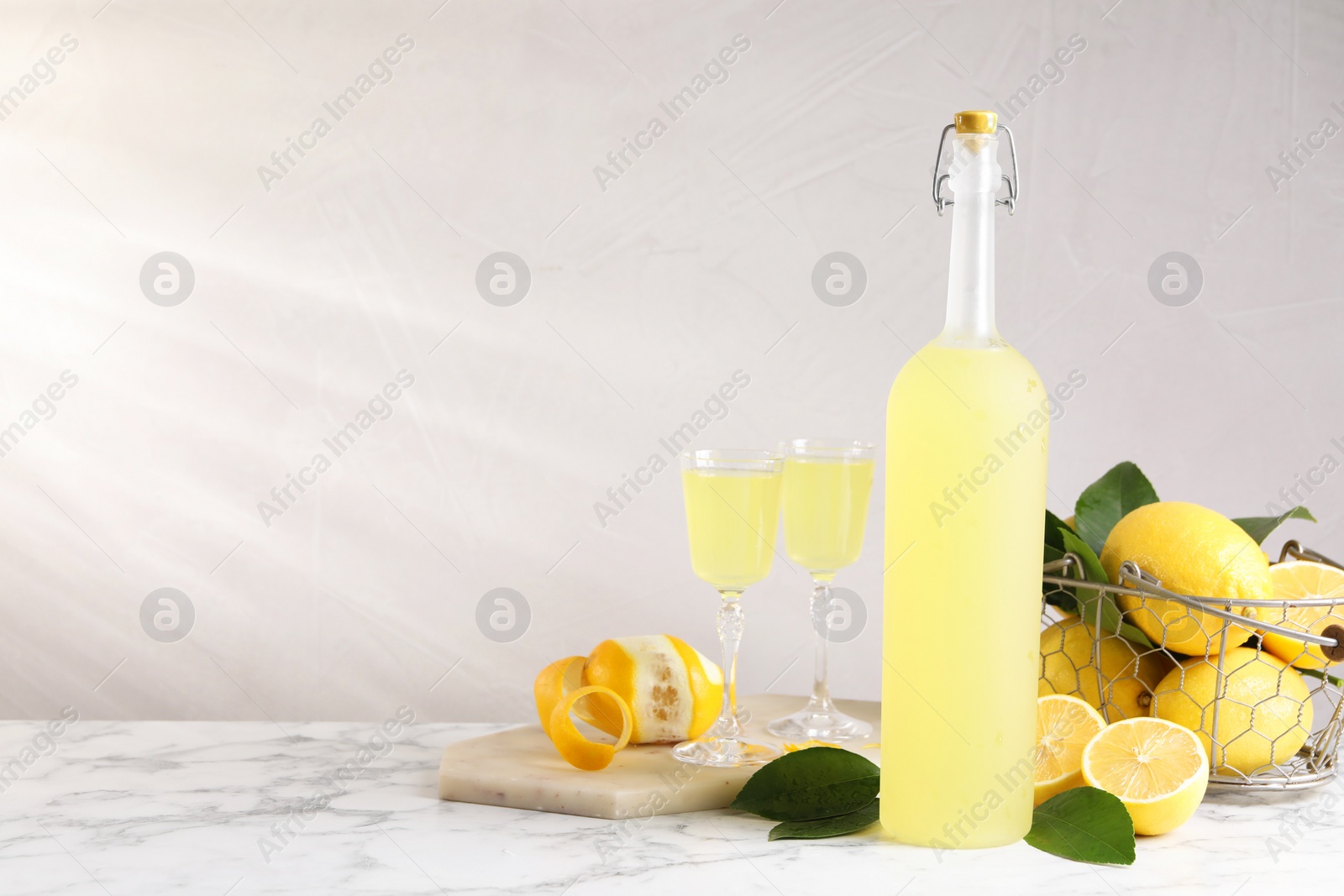 Photo of Tasty limoncello liqueur, lemons and green leaves on white marble table, space for text