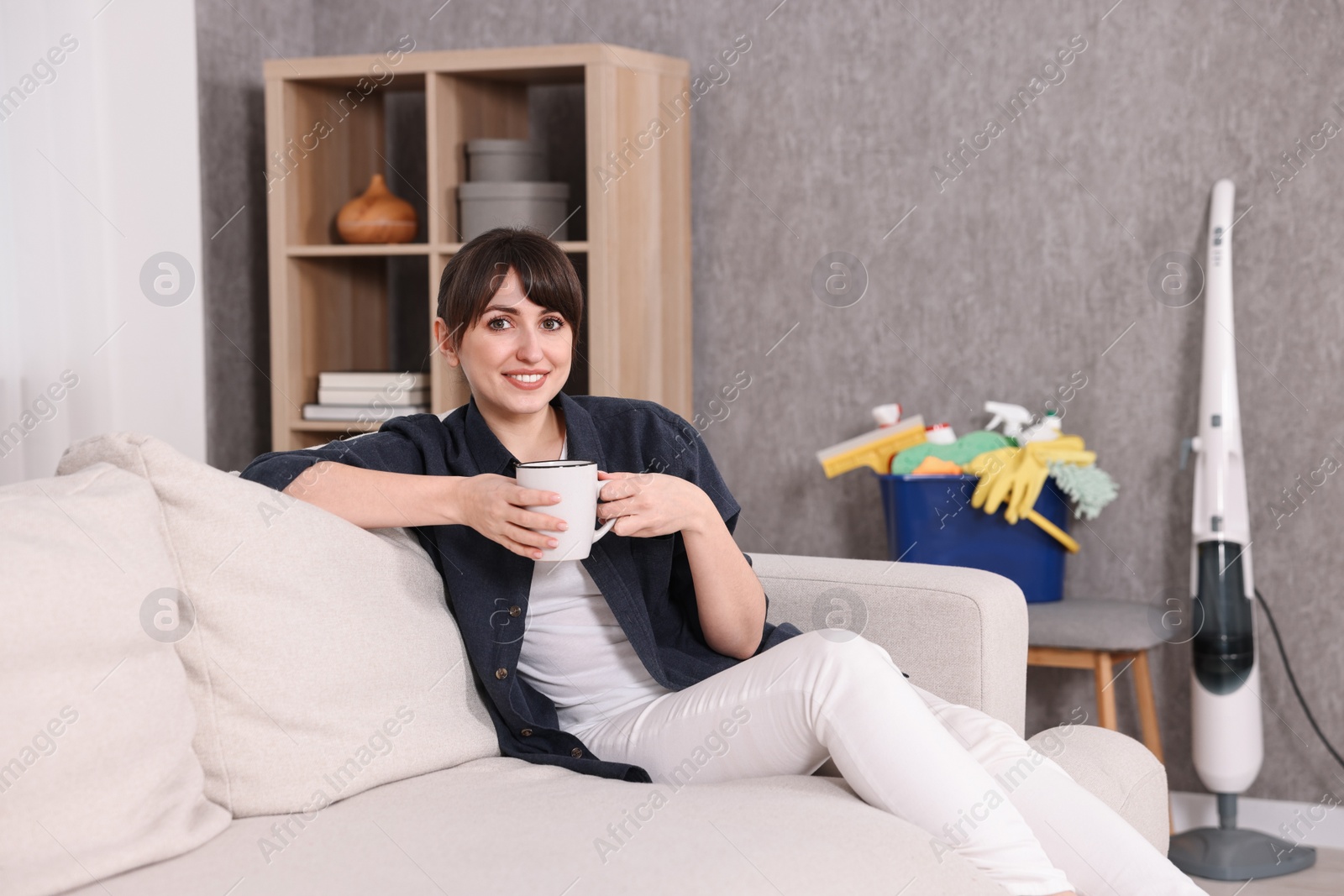 Photo of Beautiful young housewife with cup of drink resting after cleaning on sofa at home