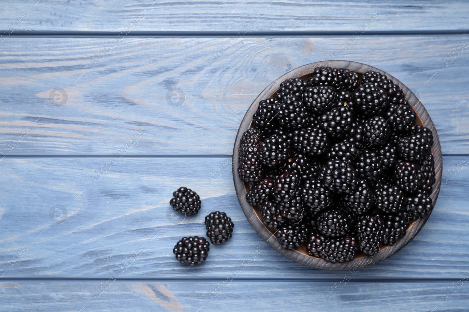 Photo of Fresh ripe blackberries on blue wooden table, flat lay. Space for text