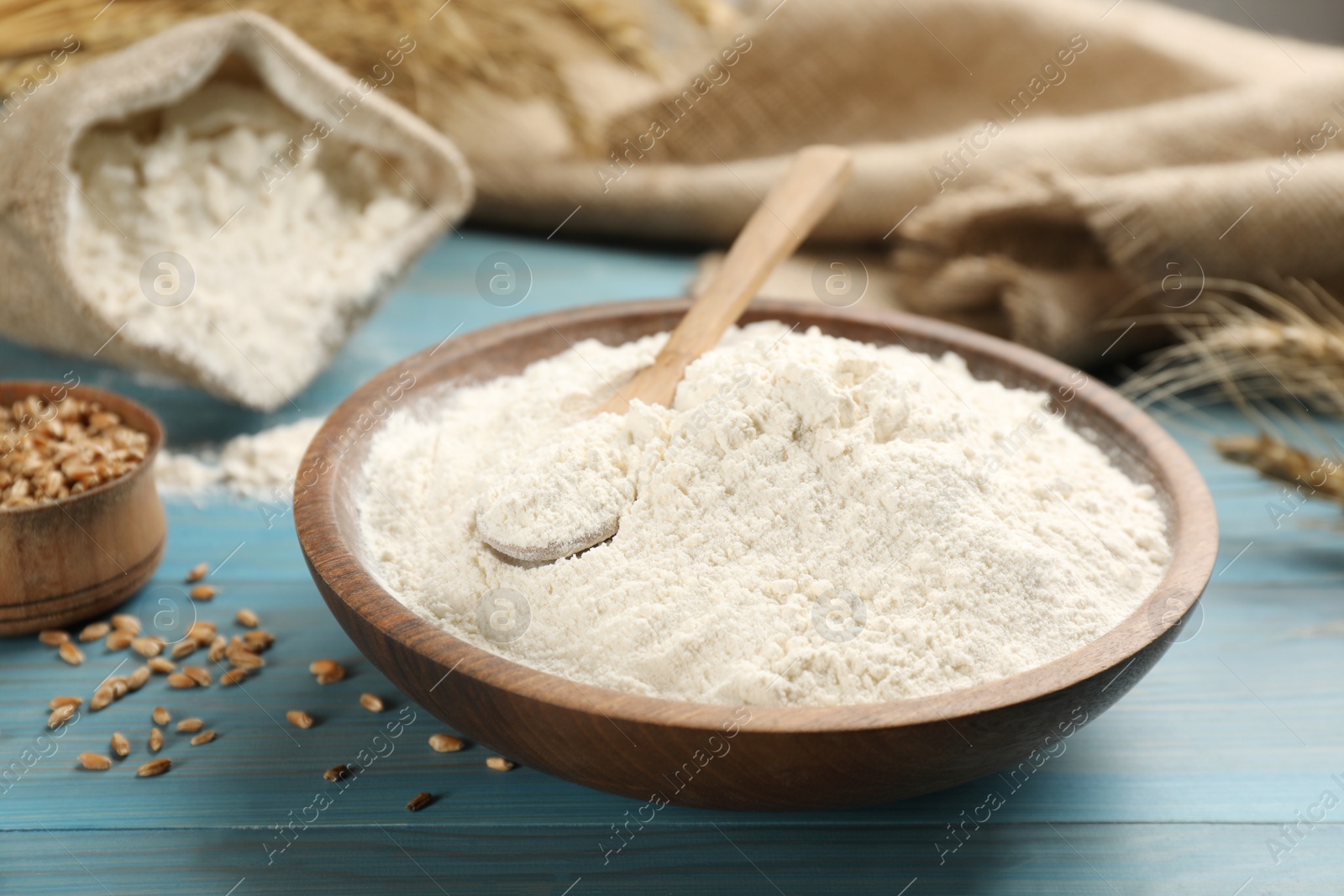 Photo of Wheat flour in bowl on light blue wooden table