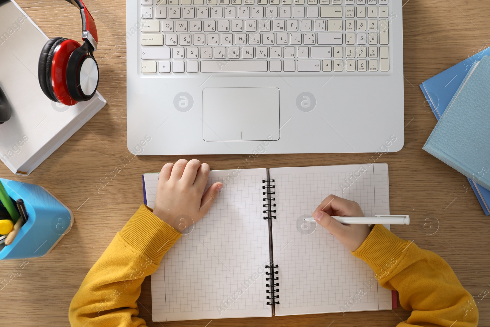 Photo of Cute little boy with modern laptop studying online at table, top view. E-learning