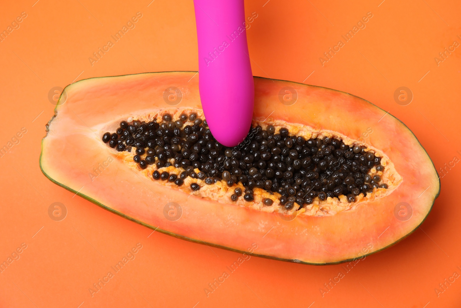 Photo of Half of papaya and purple vibrator on orange background, top view. Sex concept