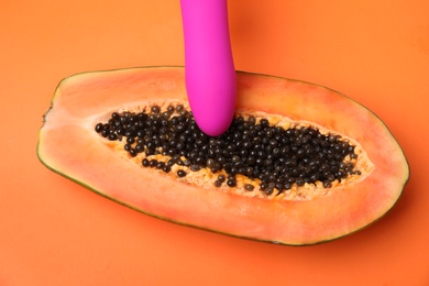 Half of papaya and purple vibrator on orange background, top view. Sex concept