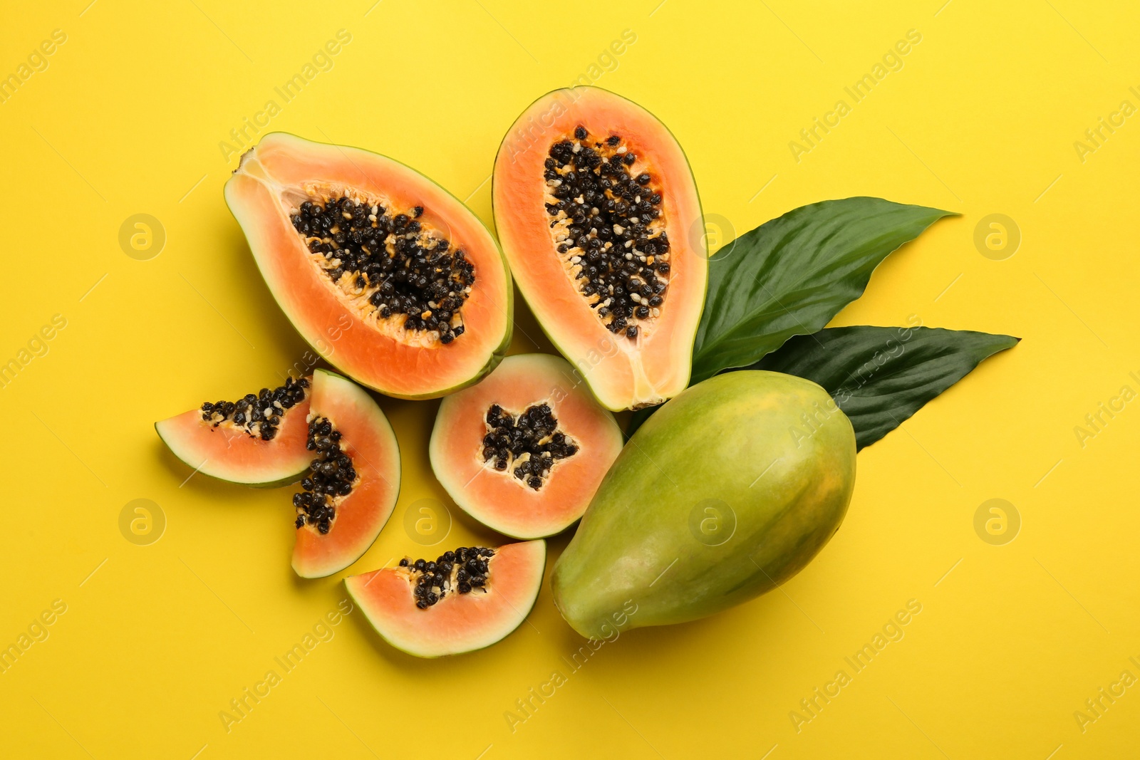 Photo of Fresh ripe papaya fruits with green leaves on yellow background, flat lay