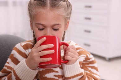 Photo of Cute girl drinking beverage from red ceramic mug at home
