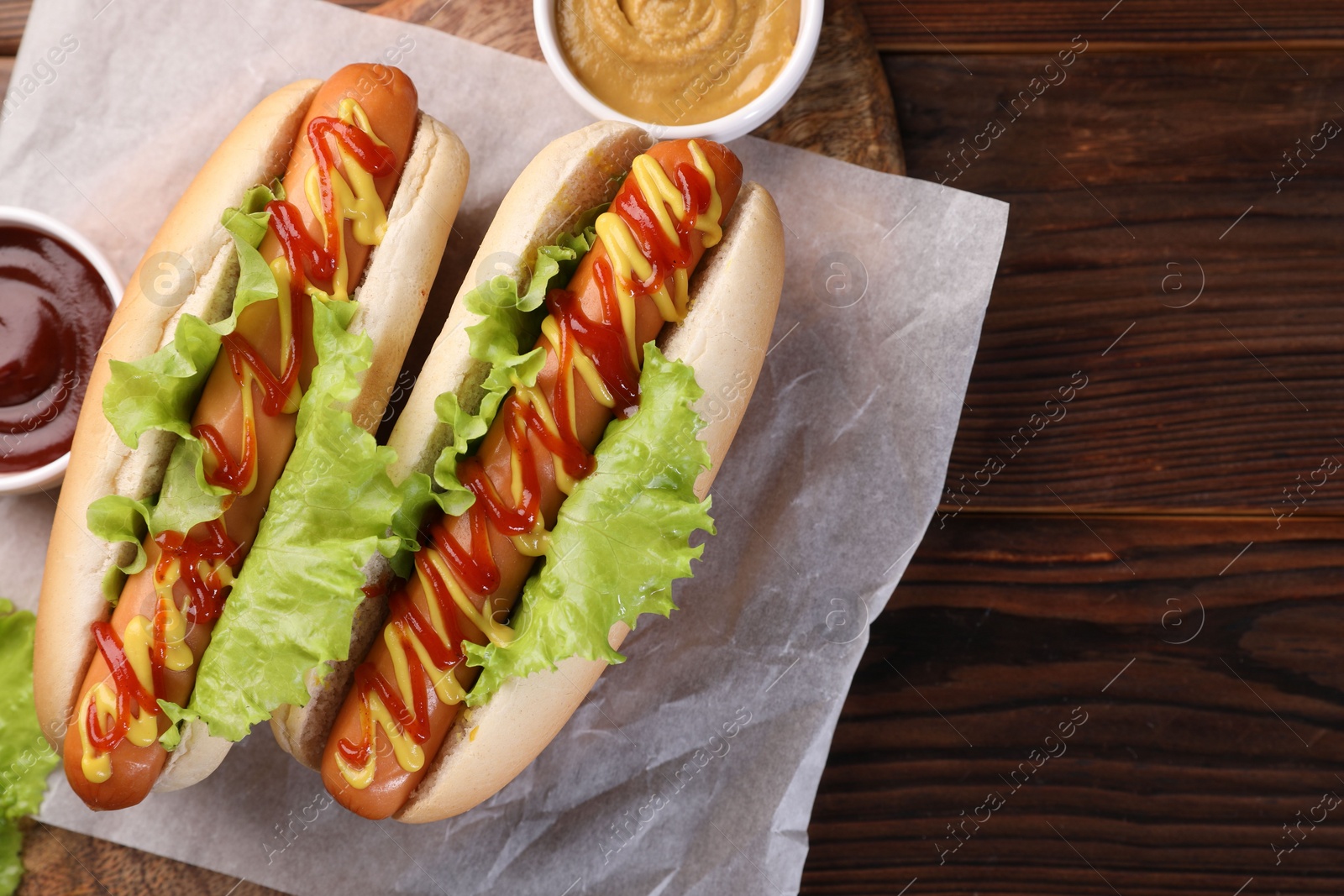 Photo of Tasty hot dogs with lettuce, ketchup and mustard on wooden table, top view. Space for text