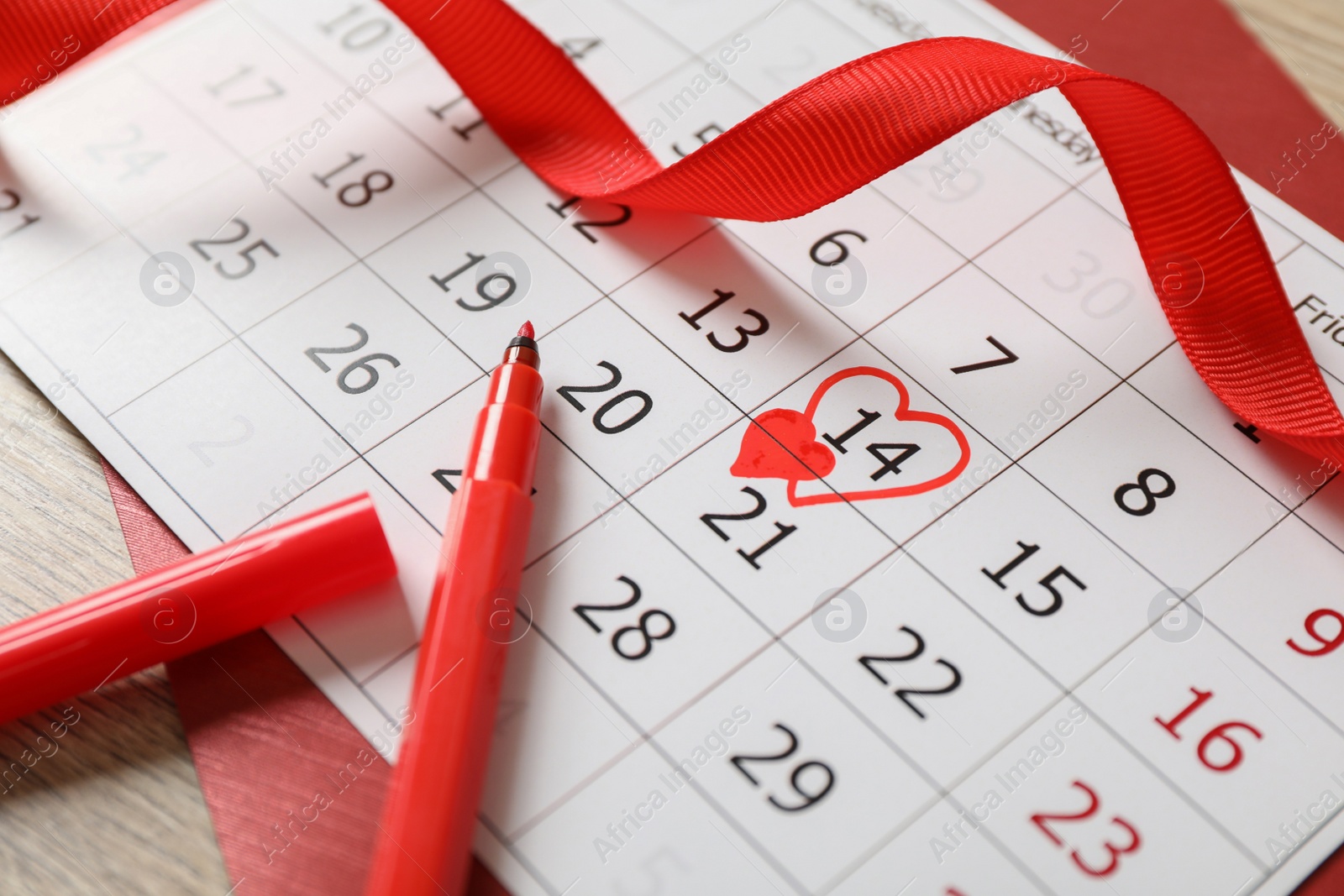 Photo of Calendar with marked Valentine's Day, red ribbon and marker on wooden table, closeup