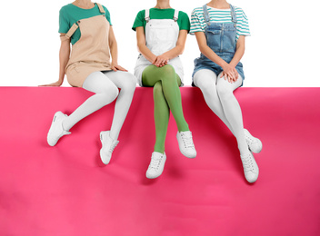 Group of women wearing colorful tights and stylish shoes sitting on color background, closeup