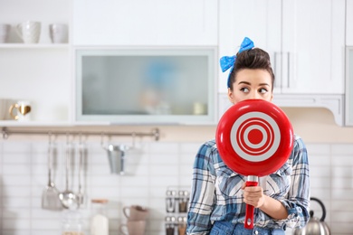 Funny young housewife with frying pan in kitchen