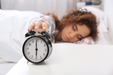 Photo of Young African-American woman turning off alarm clock at home. Bedtime