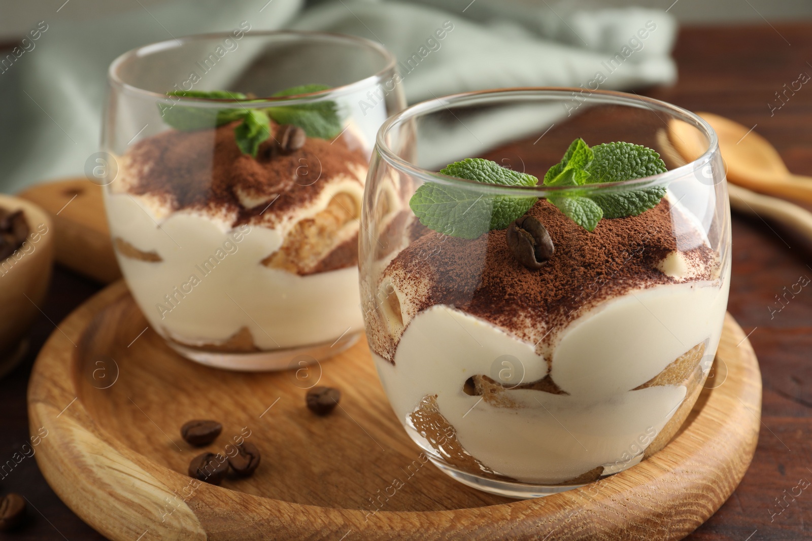 Photo of Delicious tiramisu in glasses, mint leaves and coffee beans on wooden table, closeup