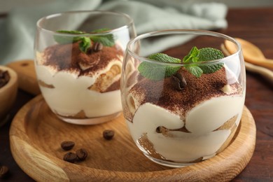 Delicious tiramisu in glasses, mint leaves and coffee beans on wooden table, closeup