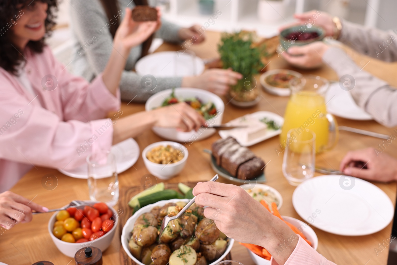 Photo of Friends eating vegetarian food at wooden table indoors, closeup