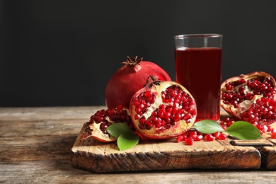 Photo of Glass of pomegranate juice and fresh fruits on wooden board against black background, space for text