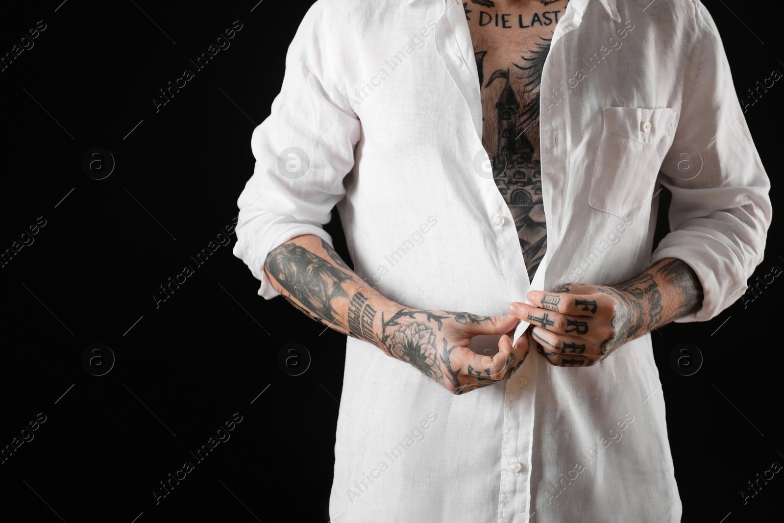 Photo of Young man with tattoos on body against black background, closeup