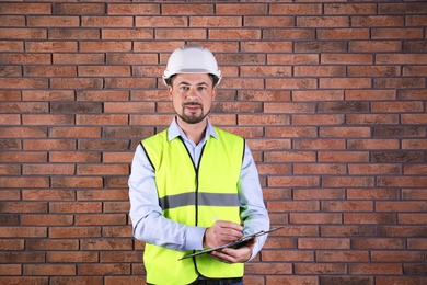 Photo of Male industrial engineer in uniform with clipboard on brick wall background. Safety equipment