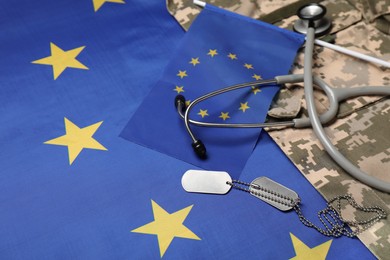 Photo of Stethoscope, tags and military uniform on flag of European Union, closeup